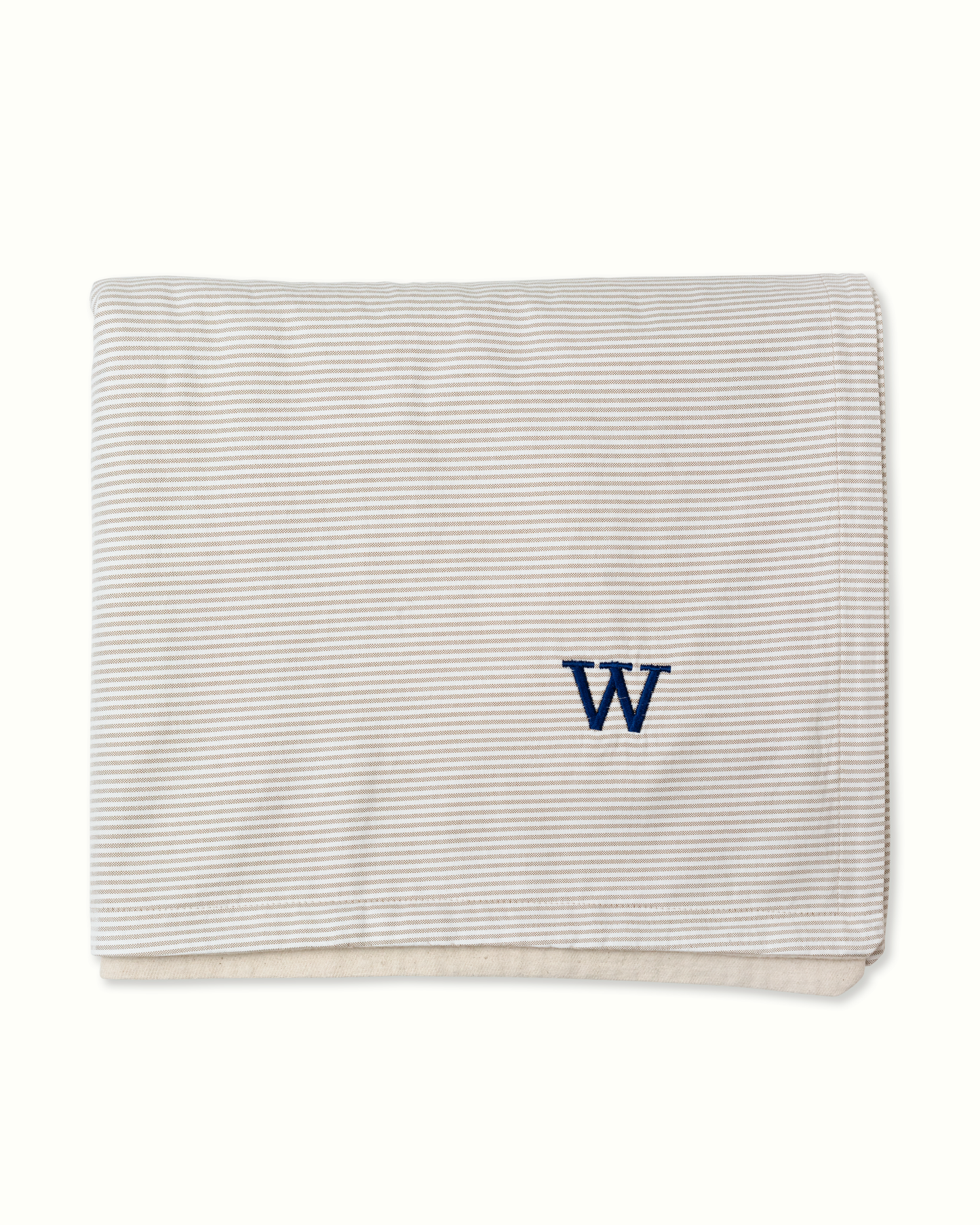 A folded cotton baby blanket with beige and white Oxford stripes and a navy blue embroidered letter 'W' on the front, set against a plain off-white background