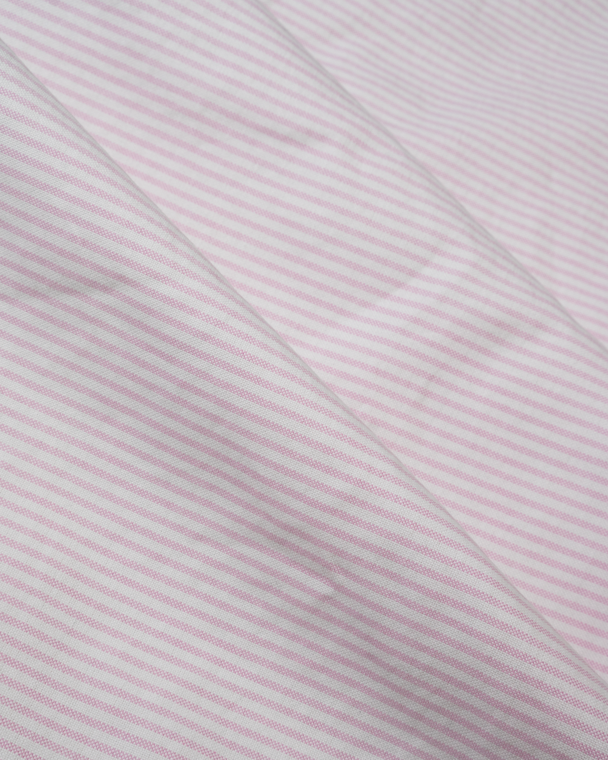 A close-up of a light pink and white Oxford stripe fabric with a fine, subtle texture and soft diagonal folds