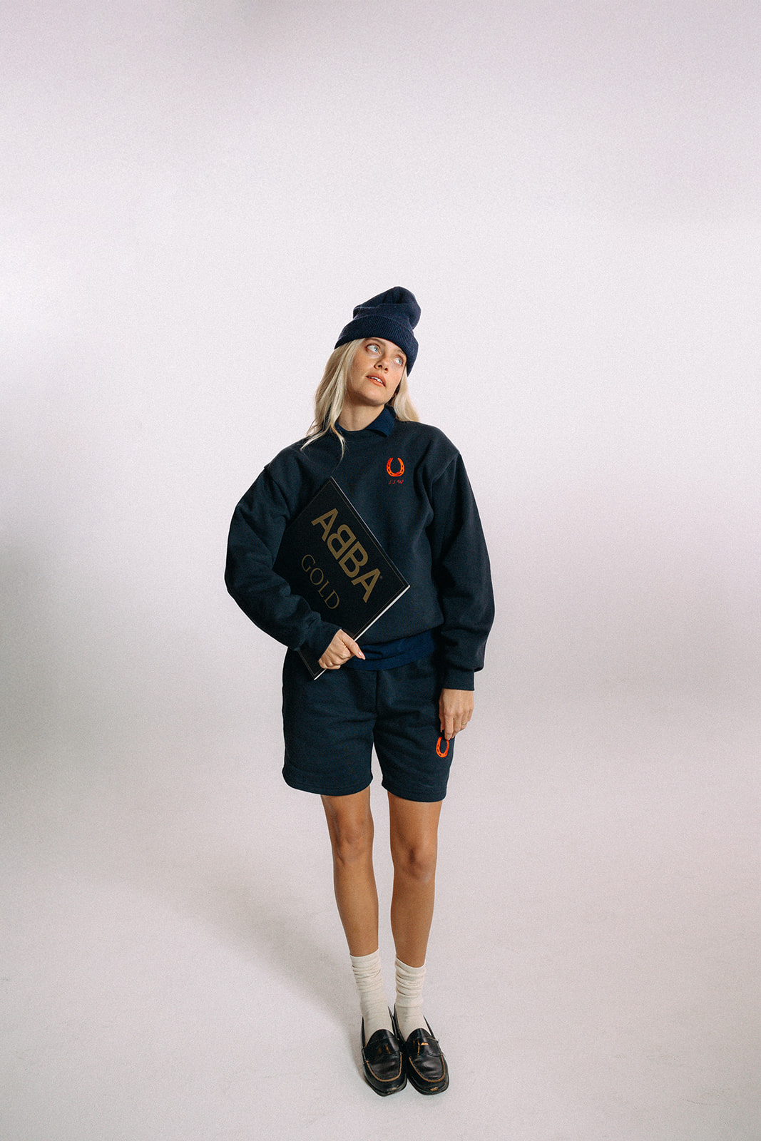 Woman wearing navy blue sweater with red horseshoe at left chest and matching shorts, white socks and black loafers